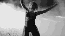 a black and white photo of a woman in a bikini dancing with her arms in the air .