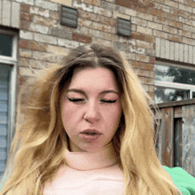 a woman with blonde hair and a nose ring stands in front of a brick wall