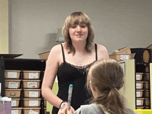 a woman in a black tank top stands next to a girl in front of a shelf with boxes labeled " puppet "