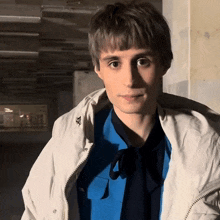 a young man wearing a white jacket and a blue shirt with a bow