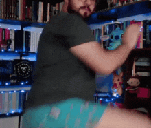 a man with a beard is dancing in front of a bookshelf with stuffed animals on it