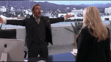 a man in a suit with his arms outstretched is talking to a woman in front of an apple computer