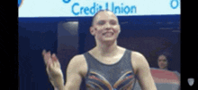 a female gymnast is waving her hand in front of a sign that says credit union