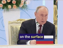 a man in a suit and tie sitting at a table with a sign that says on the surface