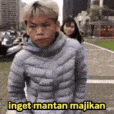 a man in a blue jacket is standing next to a woman with the words inget mantan majikan above him
