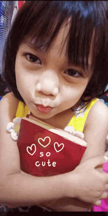 a little girl holds a red book that says so cute
