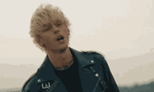 a man wearing a blue leather jacket and a black shirt is standing in front of a cloudy sky .