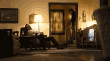 a man sits in a chair in a living room with a bottle of whiskey