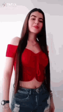 a woman with long hair is wearing a red off the shoulder crop top and jeans .