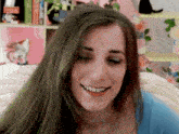 a woman with long green hair is smiling in front of a bookshelf with a cat on it