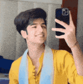 a young man in a yellow shirt is taking a selfie with his phone .
