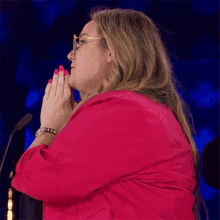 a woman wearing glasses and a pink jacket is praying in front of a microphone