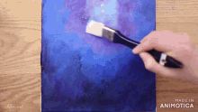 a person is using a brush to paint a blue and purple painting