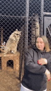 a woman is dancing in front of a chain link fence with a raccoon behind it .