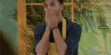 a man in a yellow apron is covering his mouth with his hands