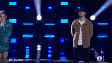 a man wearing a cowboy hat and a brown jacket stands in front of a spotlight .