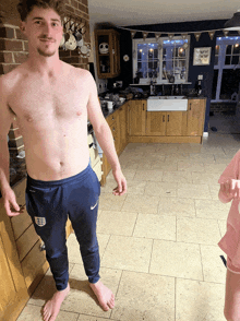 a shirtless man is standing in a kitchen wearing blue nike sweatpants