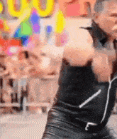 a woman in a black leather outfit is dancing in front of a colorful background .
