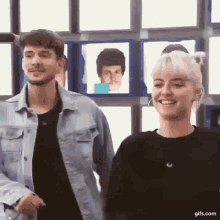 a man and a woman are standing next to each other and smiling in front of a wall of pictures .