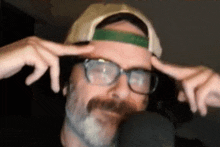 a man with a beard and glasses is wearing a hat and making a funny face in front of a microphone .