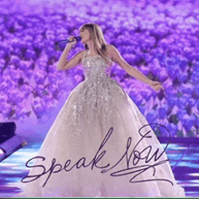 a woman in a long white dress singing into a microphone with the words speak now written below her