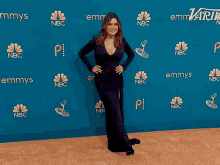 a woman in a black dress stands in front of a wall that says emmys on it