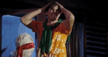 a man in a hawaiian shirt has his hands on his head .
