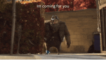 a man with a beard is walking down a street with the words i 'm coming for you below him