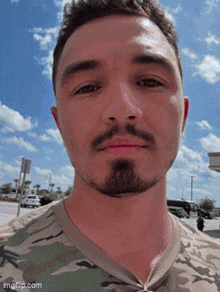 a man with a beard wearing a camo shirt looks at the camera