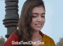 a woman is smiling in front of a sign that reads global tamilchat.com