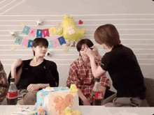 a group of young men are sitting around a table with a cake and a coca cola bottle