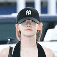 a woman wearing a new york yankees hat is standing in front of a car .