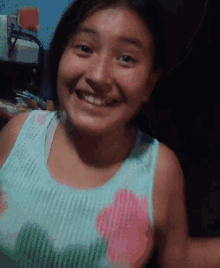 a girl wearing a blue tank top with a pink flower on it is smiling