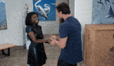a woman in a black dress shakes hands with a man in a blue shirt in front of paintings