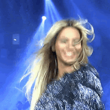 a woman with long blonde hair is smiling and dancing on a stage