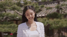 a woman wearing a white cardigan and a white top is smiling .