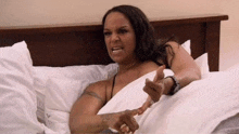 a woman in a black bra is laying in bed with white sheets and pillows .