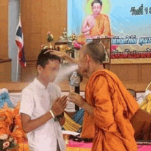 a monk is spraying water on a man 's head in a temple .