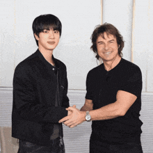 a man in a black shirt is shaking hands with a man in a black jacket