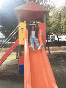 a little girl is sliding down an orange slide in a playground