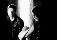 a man and a woman are standing next to each other in a room in a black and white photo .