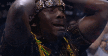 a man wearing a headband and a watch holds his hands to his head in front of a screen that says aew on it
