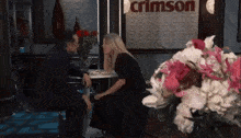 a man and woman are sitting at a table in front of a crimson sign