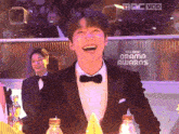 a man in a tuxedo is laughing in front of a screen that says drama awards