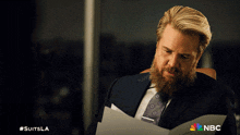 a man in a suit and tie is holding a piece of paper with nbc written on the bottom