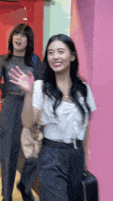 two women are walking down a hallway and one is waving at the camera