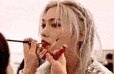 a woman with white hair is applying red lipstick with a brush