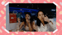 two women are sitting at a table with a box that says pcs on it