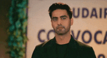 a man in a black suit and black shirt is standing in front of a sign that says udaif .