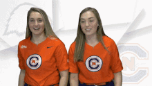 two girls wearing orange shirts with the letter c on them are standing next to each other